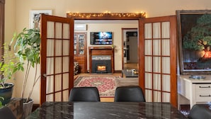 Un coin repas avec une table en marbre noir, des chaises en bois, une cheminée, un téléviseur et un tableau au mur.