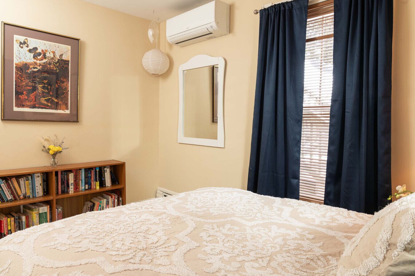 Une chambre à coucher avec un lit, une bibliothèque, un miroir et une fenêtre avec des rideaux.