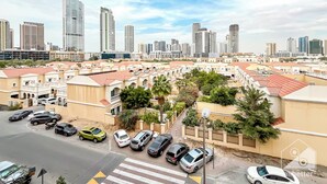 A residential area with multiple high-rise buildings, a parking lot with various cars, and a clear sky. - Vibrant Luxury Studio Emirates Gardens Dubai (Dubai)