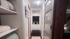 Un pasillo estrecho con piso de madera, una alfombra blanca y una ventana con plantas.