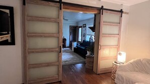 Un dormitorio con un gran ventanal corredero, una cama con cubrecama estampado, una mesita de noche con lámpara y suelo alfombrado.