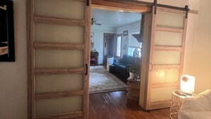 Una habitación con puerta corredera, una cama, una mesita de noche con lámpara y un pasillo que conduce a otra habitación.