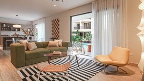 Een moderne woonkamer met een bank, fauteuil en salontafel. Achtergrond toont een keuken met een eethoek.