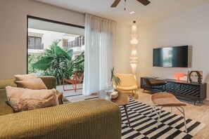 Ein modernes Wohnzimmer mit einer Couch, Sesseln, einem Fernseher und einem Balkon mit Pflanzen.