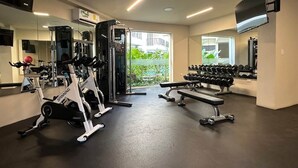 Een sportschool met cardioapparaten, een bankje, gewichten en een televisie aan de muur.