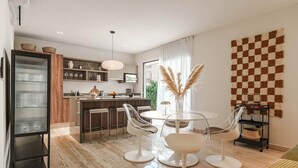 Een moderne woonkamer met een eethoek, voorzien van een keuken op de achtergrond, een groot raam met gordijnen en een geruit wandtapijt.