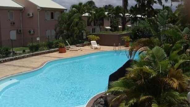 Ein Pool mit geschwungener Kante, umgeben von Palmen und einem Gebäude im Hintergrund.