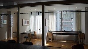 Una habitación moderna con separador de vidrio, suelo de madera y zona de comedor con sillas y una mesa.