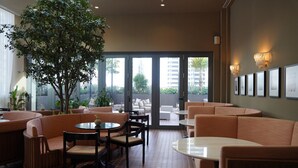 Un espacio interior moderno con zonas de estar, un árbol grande y vistas al exterior a través de puertas de cristal.