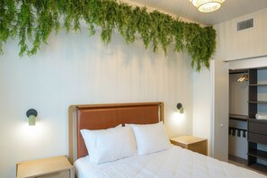 A hotel room with a bed, nightstands, a wall-mounted plant, and a closet. - 2BR/2BA Palm Oasis at The Crosby (Miami)