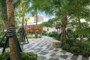 A courtyard with a checkered floor, palm trees, and a building with large windows in the background. - 2BR/2BA Palm Oasis at The Crosby (Miami)