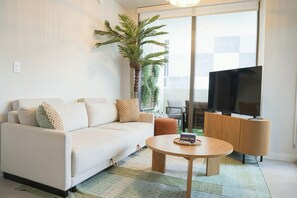 A modern living room with a sofa, a coffee table, a television, and a large window. - 2BR/2BA Palm Oasis at The Crosby (Miami)