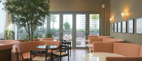 A modern interior with seating areas, a large tree, and a view through glass doors.