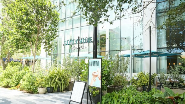 An outdoor seating area with a sign for 'SIXTY VINE Wine & Dine' and a menu board. - 2BR/2BA Palm Oasis at The Crosby (Miami)