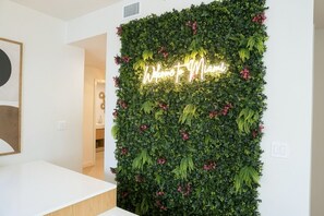 A reception area with a wall-mounted green foliage display and a neon sign that reads 'Welcome to Miami.' - 2BR/2BA Palm Oasis at The Crosby (Miami)