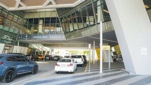 A modern building with a glass facade, a sign for 'Central Fare' and 'Brightline', and a drop-off zone. - 2BR/2BA Palm Oasis at The Crosby (Miami)