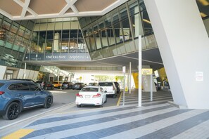 A modern building with a glass facade, a sign for 'Central Fare' and 'Brightline', and a drop-off zone. - 2BR/2BA Palm Oasis at The Crosby (Miami)