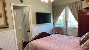 Quarto com cama, televisão na parede, janela com cortinas e porta.