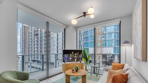 Een moderne woonkamer met een groot raam, een flatscreen televisie, een ronde salontafel en een bank met kussens.