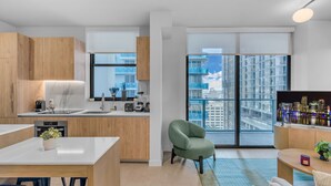 Een moderne keuken met een groot raam, een eethoek met een tafel en stoelen, en een zithoek met een bank en een fauteuil.