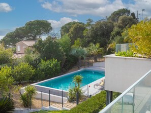 Une piscine entourée d’une végétation luxuriante et un bâtiment moderne.