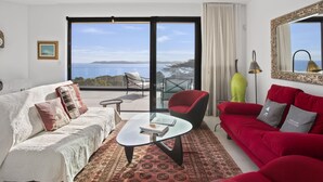 Een ruime woonkamer met een grote schuifpui naar een balkon met uitzicht op zee.