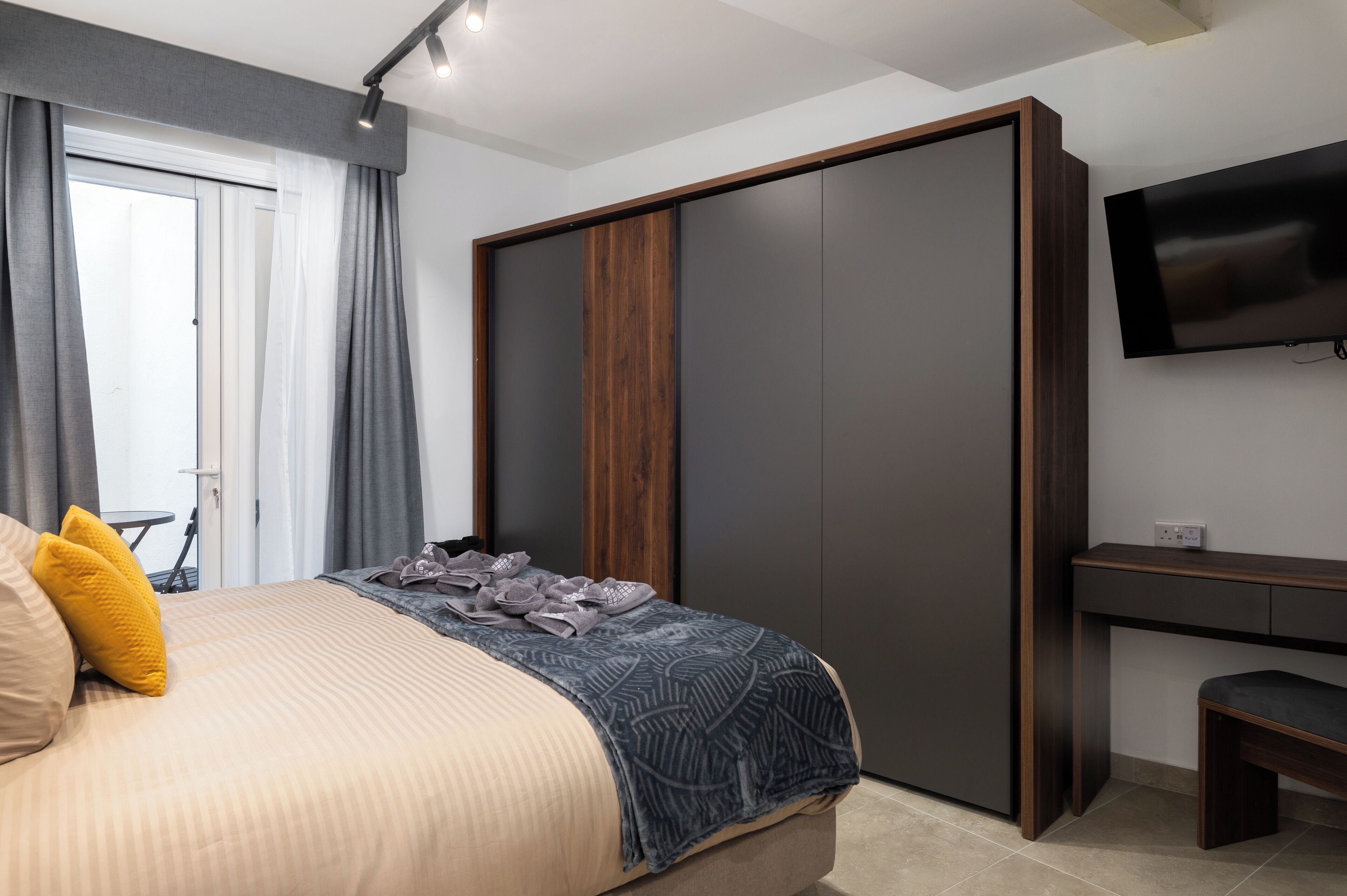 A bedroom with a bed, a wardrobe, a desk, and a TV.