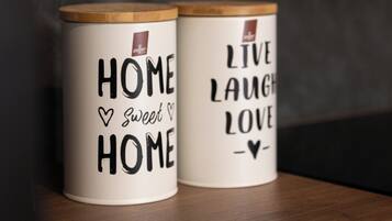 Due tazze di ceramica bianca con coperchi in legno, una con la scritta “HOME SWEET HOME” e l’altra con “LIVE LAUGH LOVE”.