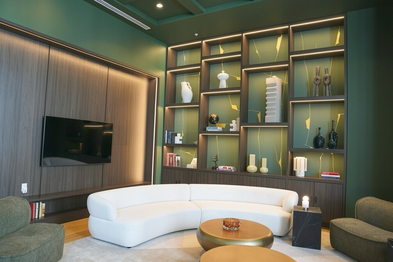 Een moderne woonkamer met een gebogen witte bank, een flatscreen televisie aan de muur en een inbouw wandplank met decoratieve objecten.