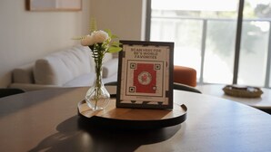 Ein Tisch mit einem gerahmten QR-Code, einer Blumenvase und einer Couch im Hintergrund.