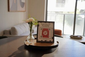 A table with a framed QR code, a vase with flowers, and a couch in the background. - Stylish Minimalist 1BR in The Crosby (Miami)