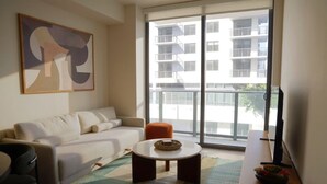 Ein Wohnzimmer mit einer Couch, einem Couchtisch, einem Fernseher und einem Balkon mit Blick auf Gebäude.