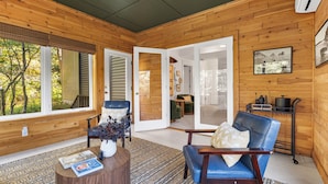 Ein Holzinterieur mit einem blauen Ledersessel, einem kleinen Tisch mit Büchern und Blick ins Freie durch große Fenster.
