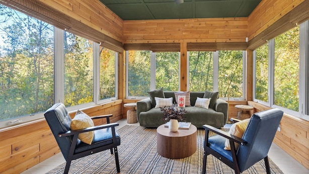 Ein gemütlicher Raum mit Holzbalkendecke, großen Fenstern, einer Couch, zwei Sesseln und einem Couchtisch.