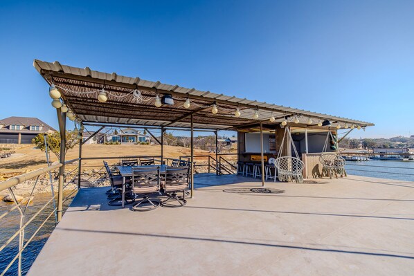 An outdoor patio with tables and chairs, a covered seating area, and a view of a body of water. - Sunset @ PK Lakefront Retreat w/Private Boat Dock - Near Rocker B Ranch (Graford)