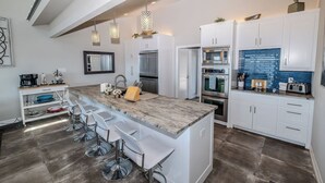 A modern kitchen with white cabinets, a large island with bar stools, stainless steel appliances, and pendant lighting.