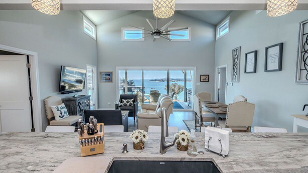 A modern kitchen with a marble countertop, a built-in sink, and a ceiling fan. There are two windows providing natural light and a view of the outdoors.