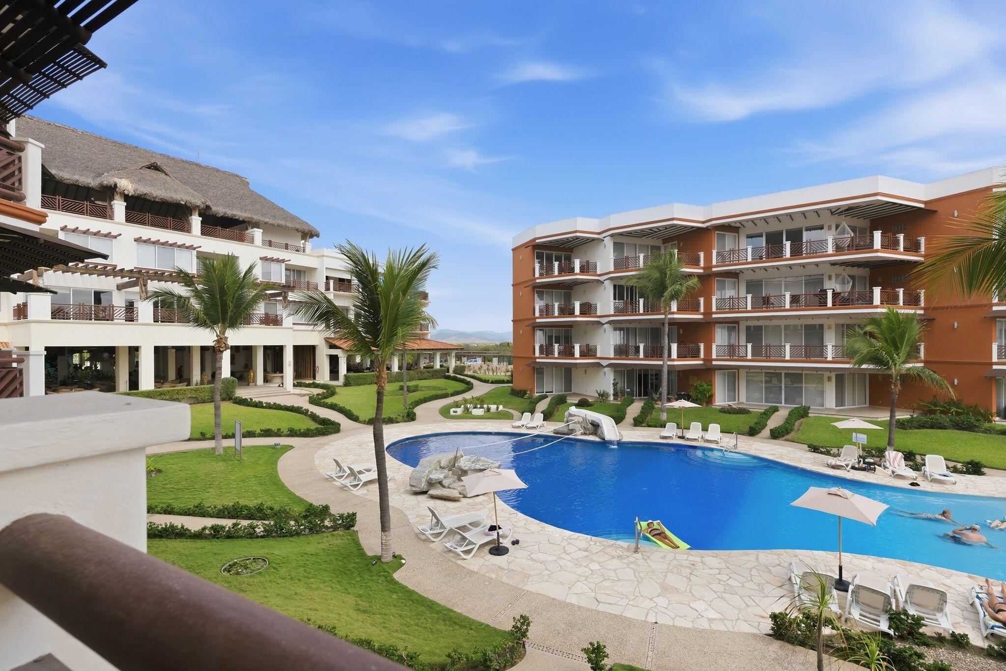 A resort with a central pool, multiple balconies, and lush landscaping.