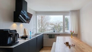 A modern kitchen with a built-in stove, a coffee machine, and a window with a view of trees. - 2 bedroom cozy apartment in Broek in Waterland (Broek in Waterland)