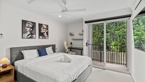 Quarto moderno com uma cama grande, ventilador de teto e porta de vidro deslizante para uma varanda com vista para o verde.