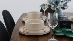 Uma mesa de jantar posta com pratos, tigelas e uma taça de vinho, acompanhada por um vaso de flores.