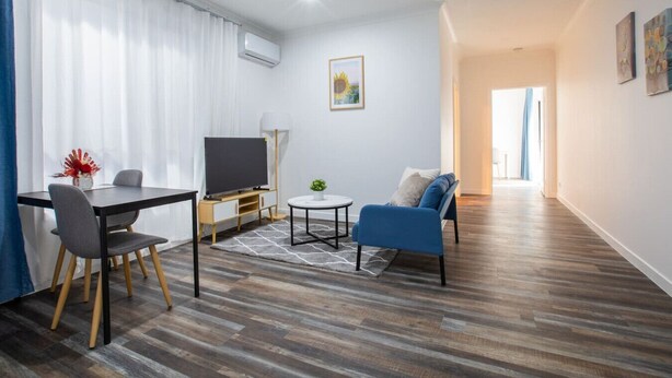 Ein modernes Wohnzimmer mit Flachbildfernseher, einem Esstisch mit Stühlen, einer Couch und einem kleinen runden Tisch mit Pflanze.