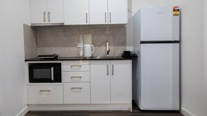 Eine kleine Küche mit weißen Schränken, einem eingebauten Backofen, einem Kühlschrank und einer Kaffeemaschine auf der Arbeitsplatte.