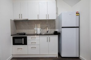 A compact kitchen with white cabinets, a built-in oven, a refrigerator, and a coffee maker on the countertop. - 1BR Unit | Private Bathroom Kitchen & living area (Oxley)