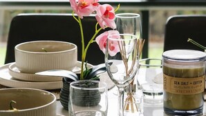 A dining table set with plates, bowls, glasses, and cutlery, with a candle and orchid flowers on the table. - 3BR Family Home in Rochedale | Aussie Local Living (Rochedale)