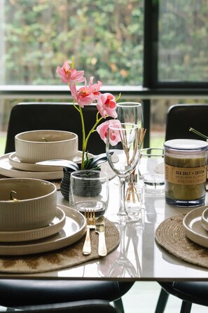 A dining table set with plates, bowls, glasses, and cutlery, with a candle and orchid flowers on the table. - 3BR Family Home in Rochedale | Aussie Local Living (Rochedale)
