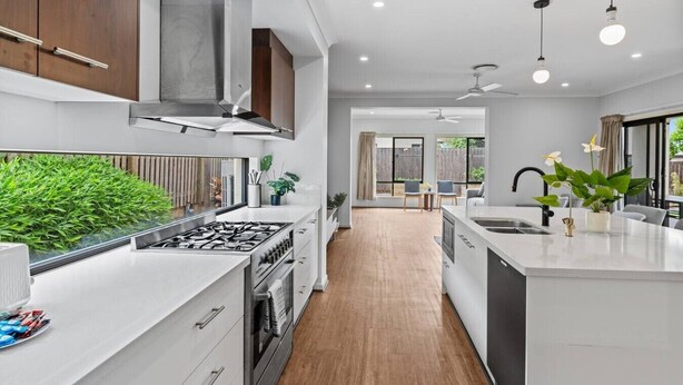 A modern kitchen with a central island, built-in oven, and a large window overlooking a garden. - 3BR Family Home in Rochedale | Aussie Local Living (Rochedale)