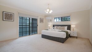 A bedroom with a large bed, a nightstand, a chandelier, and a sliding glass door. - Spacious 5BR Family Home with Pool in Robertson (Robertson)