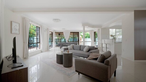 A spacious living room with a large grey sofa, a coffee table, and a flat-screen TV on a wooden stand. - Spacious 5BR Family Home with Pool in Robertson (Robertson)