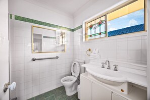A bathroom with white tiles, a toilet, a sink with a mirror, and a window with a stained glass design. - Modern 4B Family-Friendly Home in Robertson QLD (Robertson)